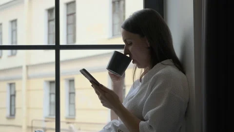Female in Bathrobe Using Smartphone on Windowsill Video stock 162824339