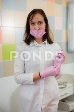 A female beautician in a pink medical mask and pink disposable gloves Stock Photos