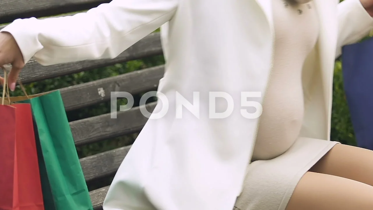 Female with big belly sitting on bench after shopping, baby clothing sale