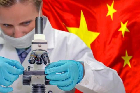Female biochemist looking through a microscope against China flag background. Stock Photos