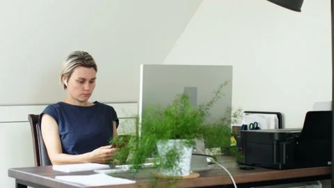 Female in blue using smartphone in hands while sitting desk computer monitor Stock Footage 237894942