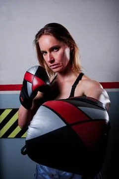 Female boxer looking at camera while posing with boxing gloves indoors. Stock Photos