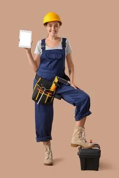 Female builder with blank tablet computer and tools on beige background Stock Photos