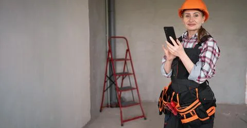 Female builder chatting message on her mobile phone standing in new build hou Stock Photos