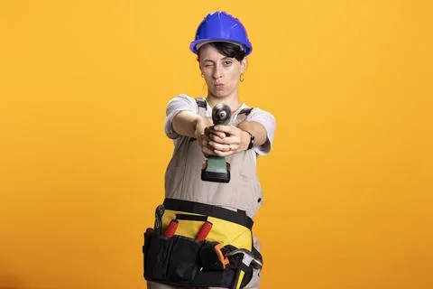 Female builder holding construction tool and posing playfully in studio Stock Photos
