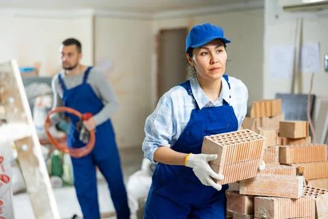 Female builder stacking red bricks at construction site indoors Stockfoto's