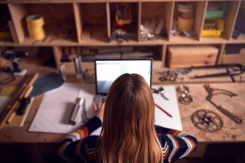 Female Business Owner Working Late In Carpentry Workshop Using Laptop Stock Photos