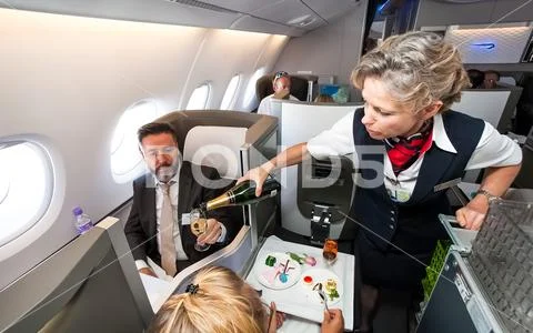 Female cabin crew pouring a glass of champaign in business class of an Airbus Stock Photos