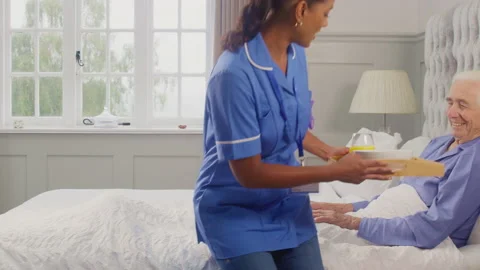 Female Care Worker In Uniform Bringing Senior Man At Home Breakfast In Bed On Stock Footage