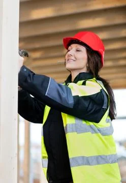 Female Carpenter In Reflective Jacket Using Hammer At Site Foto stock