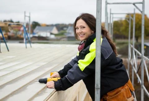 Female Carpenter Smiling While Holding Drill Machine At Roof Stock Photos