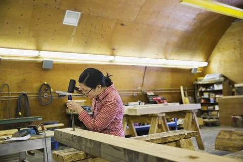 Female carpenter using mallet and chisel at workshop Foto stock