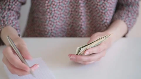 Female Caucasian hands at the table count dollar bills and write in a notebook. Stock Footage 154350809
