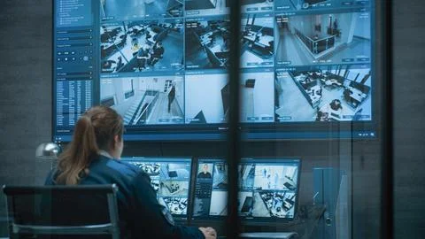 Female CCTV operator works on computer with security cameras, talks on walkie Foto stock