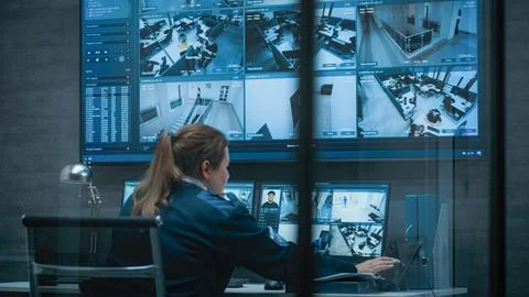 Female CCTV operator works on computer with security cameras, talks on walkie Foto stock