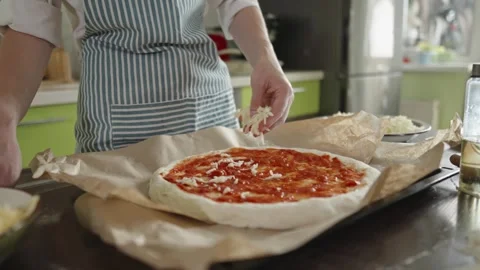 Female chef in an apron is putting mozzarella cheese on a raw pizza Stock Footage 280157770