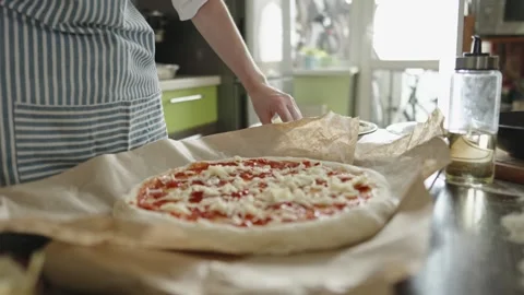 Female chef in an apron is putting mozzarella cheese on a raw pizza Stock Footage 280157793