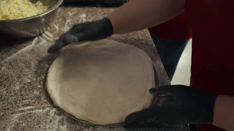 Female chef in black gloves skillfully rolls out dough on a granite countertop, Vídeo Stock 332736628