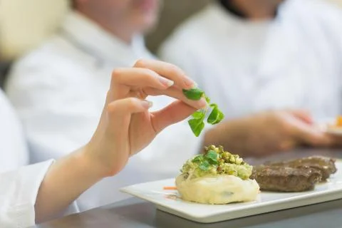 Female chef garnishing a plate with steak Stock Photos