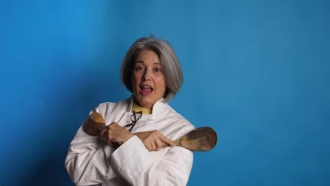 Female chef hiding face behind wooden spoons and smiling at camera Vidéo 341336032