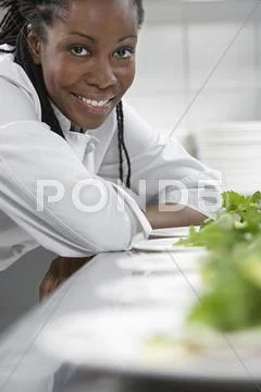 Female Chef With Plates Of Salads In Kitchen Stock Photos