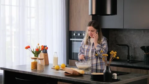 Female chef prepares pancake dough according to recipe on phone in kitchen Stock Footage 277400012