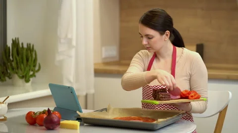Female chef preparing a pizza and watching recipes online on platform for watchi Stock Footage 148647280