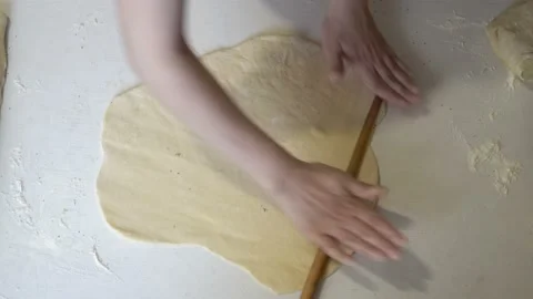 A female chef rolls out a thin layer of dough with a wooden rolling pin in the Stock Footage 145545911