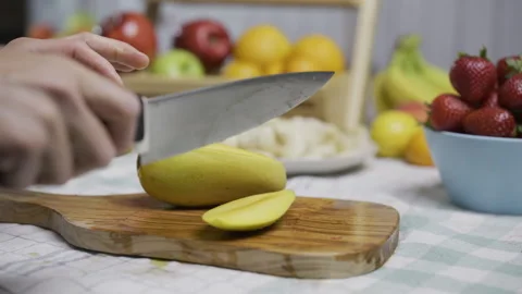 Female chef using knife to cut up juicy mango in kitchen - closeup Stock Footage 341226344