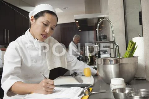 Female Chef Writing On Clipboard In Kitchen Stock-Fotos