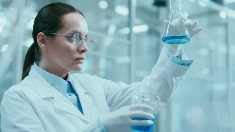 Female Chemist Examining Blue Liquid in Flask during Laboratory Experiment Vidéo 331337553