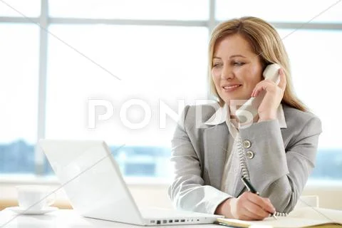 Female chief speaking by telephone and writing something while looking at laptop Stock Photos