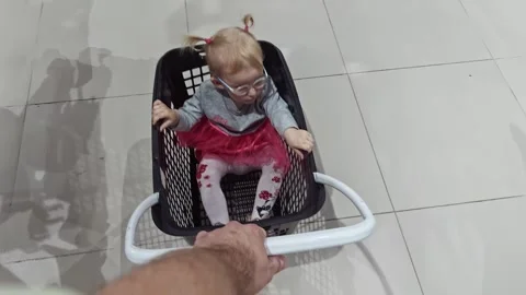 Female child in spectacles sits inside plastic shopping cart being pulled along Video stock 315511150