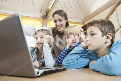 Female childcare assistant and three boring children looking at laptop Stock Photos