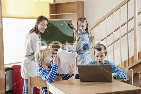 Female childcare assistant helping children by doing homework Stock Photos