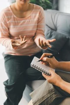 Female client explains feelings with open hands while therapist writes in n.. Stock Photos