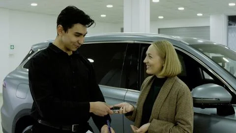 Female client looking down at documents next to a new car in the showroom Stock-Fotos