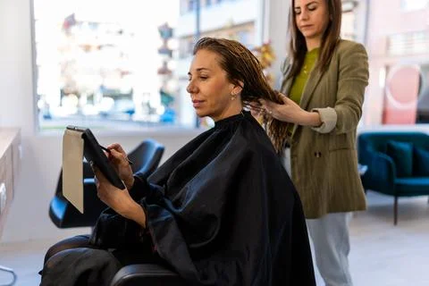 Female client using tablet while hairdresser brushing hair Stock Photos