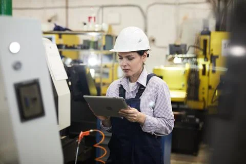 Female cnc machine operator checking setups on tablet Stock Photos