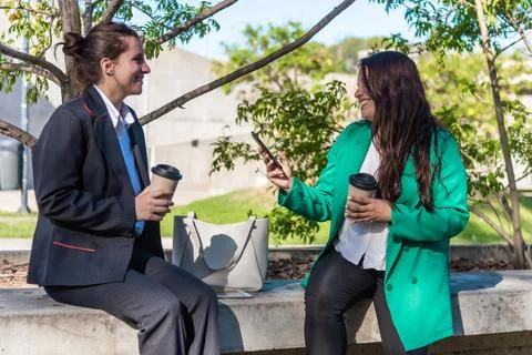 Female co-workers talking while relaxing outdoors during a coffee break. Stock Photos