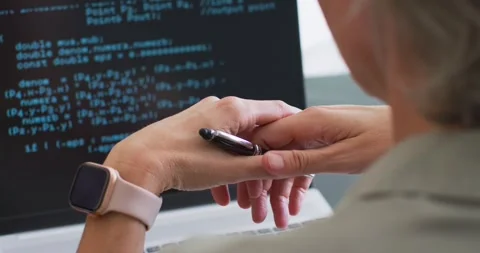 Female coder at desk seeing code on laptop, adjusting black pen and smartwatch, Stock Footage 336569646