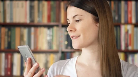 Female college student using mobile in university library, browsing, reading Stock Footage 89586942