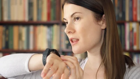 Female college student using smart watch in library, dictating audio message to Video stock 87615763