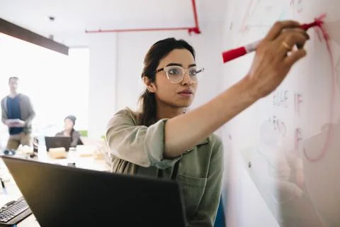 Female computer programmer with laptop writing on whiteboard in office Stock Photos