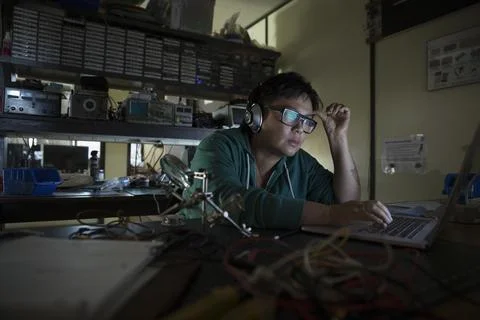Female computer programmer working at laptop wearing headphones in dark workshop Stockfoto's