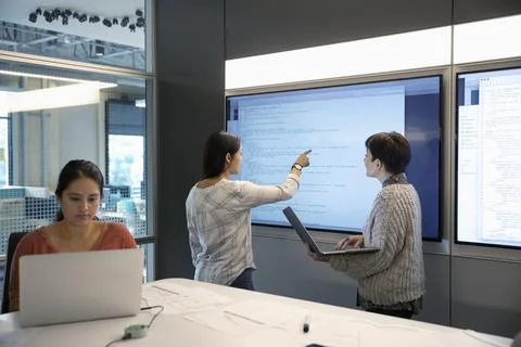 Female computer programmers with laptops reviewing code on touch screen in confe Stock Photos