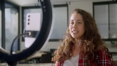 Female content creator or vlogger talking to phone lit by ring light in her home Stock Footage 311766534