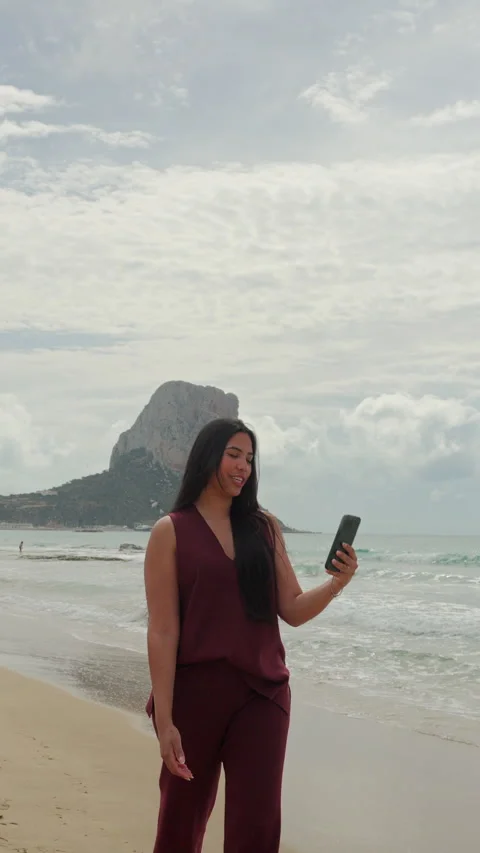 Female content creator streaming live on her phone while walking on the shore Stock-Footage 333690513