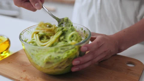 Female cook's hands stirring spaghetti in a glass bowl stirring with green s Stock Footage 219863281