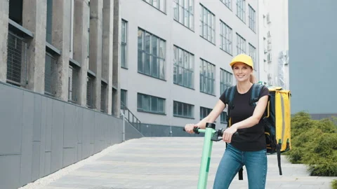 Female courier with yellow backpack on an electric scooter. Fast delivery in Stock Footage 171892425